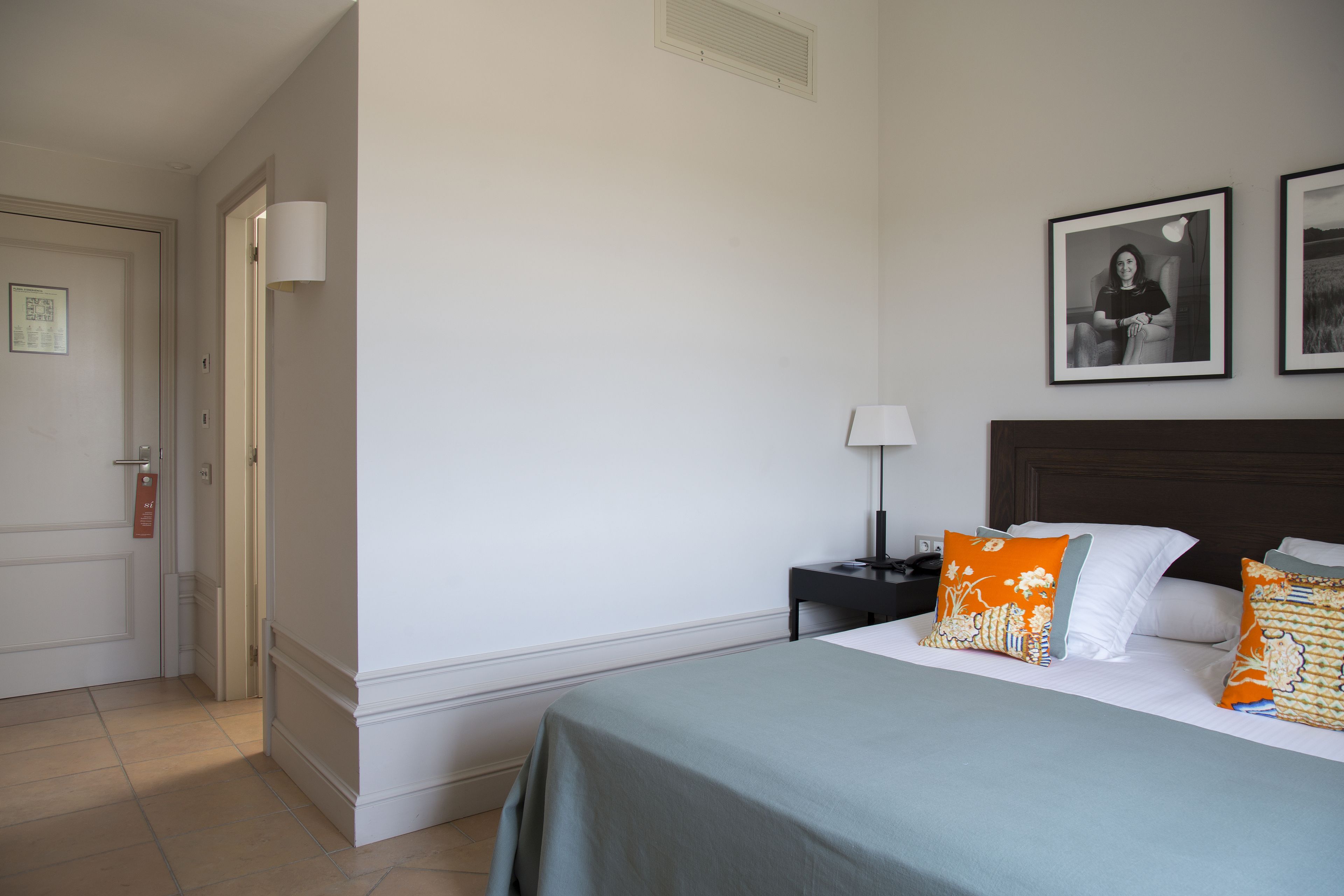 A hotel room with a bed, a nightstand, a lamp, and two framed pictures on the wall.