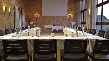 A conference room with a long table, chairs, a projector screen, and a stone wall.