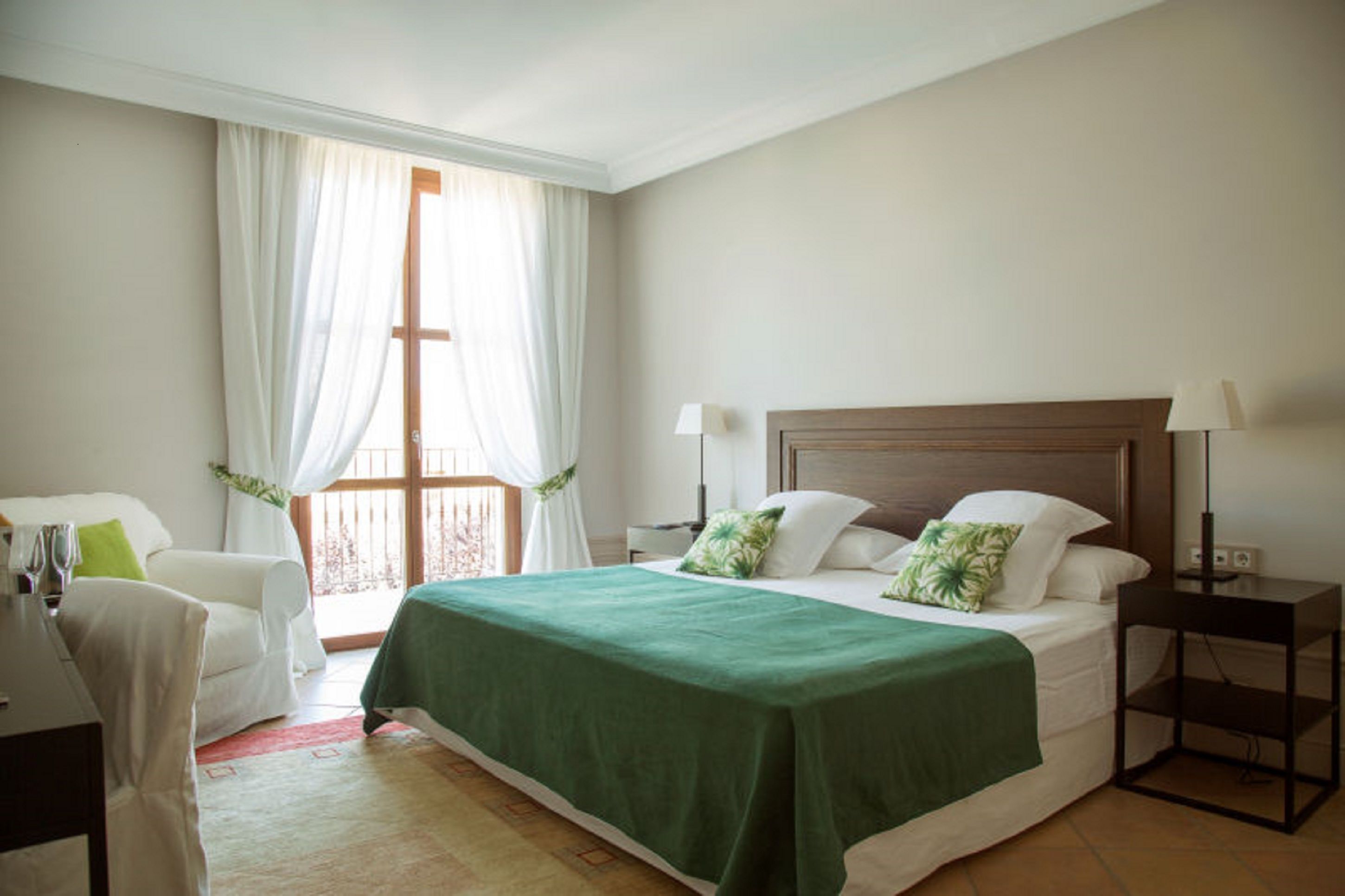 A hotel room with a bed, a chair, a nightstand, and a window with curtains.