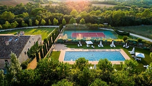 Vista aérea de una propiedad con piscina, canchas de tenis y un patio con sillas de descanso.