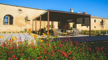 A stone building with a covered patio area, outdoor seating, and a garden with red flowers.