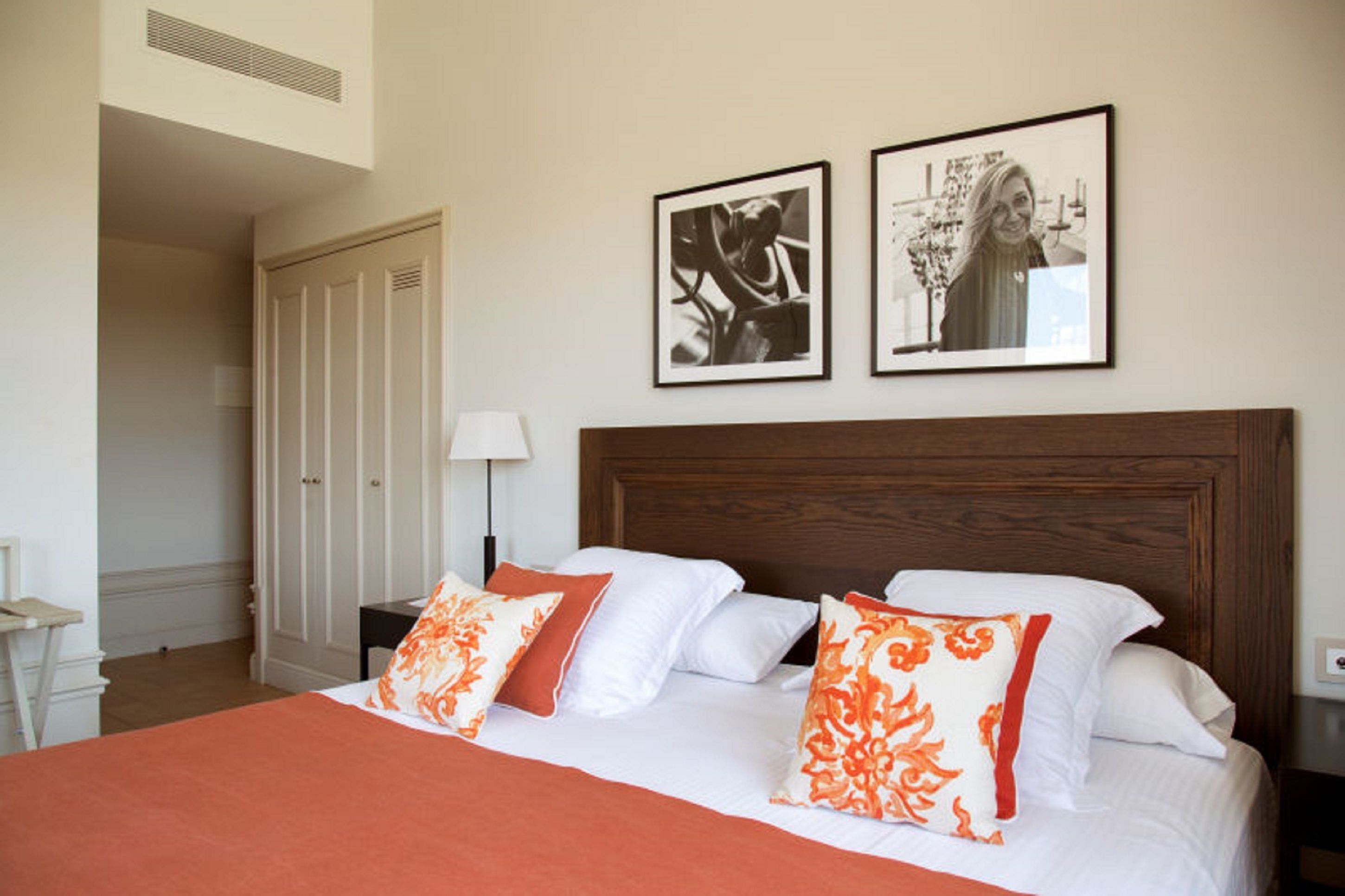 A hotel room with a large bed, two pillows, a nightstand, a lamp, and two framed pictures on the wall.