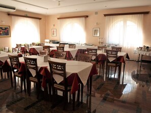 A dining area with multiple tables and chairs, arranged in a spacious room with large windows and a tiled floor. - Villa Armin (Rovinj)