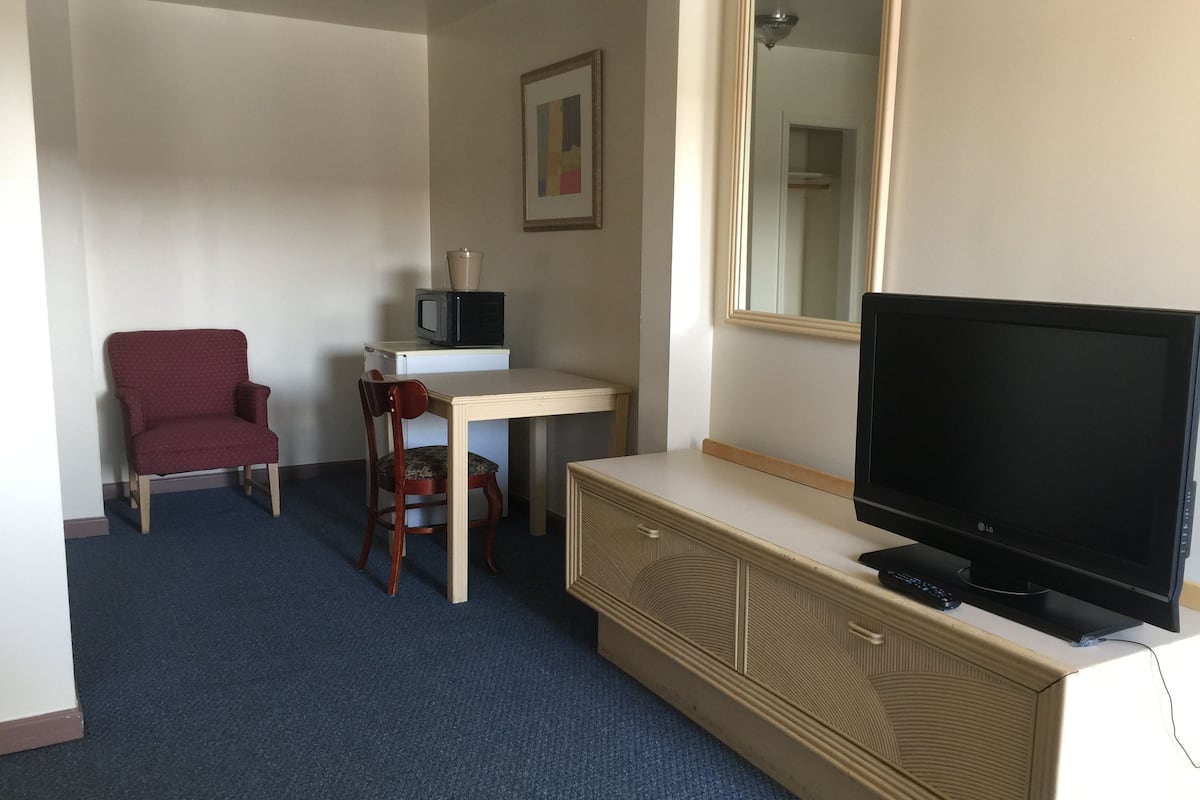 A hotel room with a red armchair, a small desk with a microwave, a television, and a dresser.