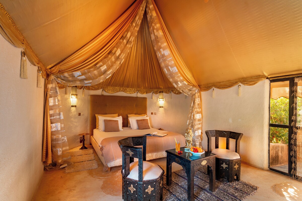 A tented room with a bed, two chairs, a table, and a nightstand.
