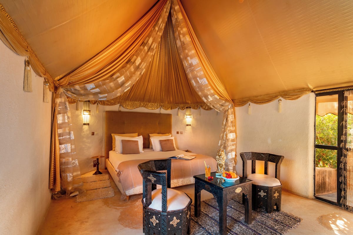 A tented room with a bed, two chairs, a table, and a nightstand.