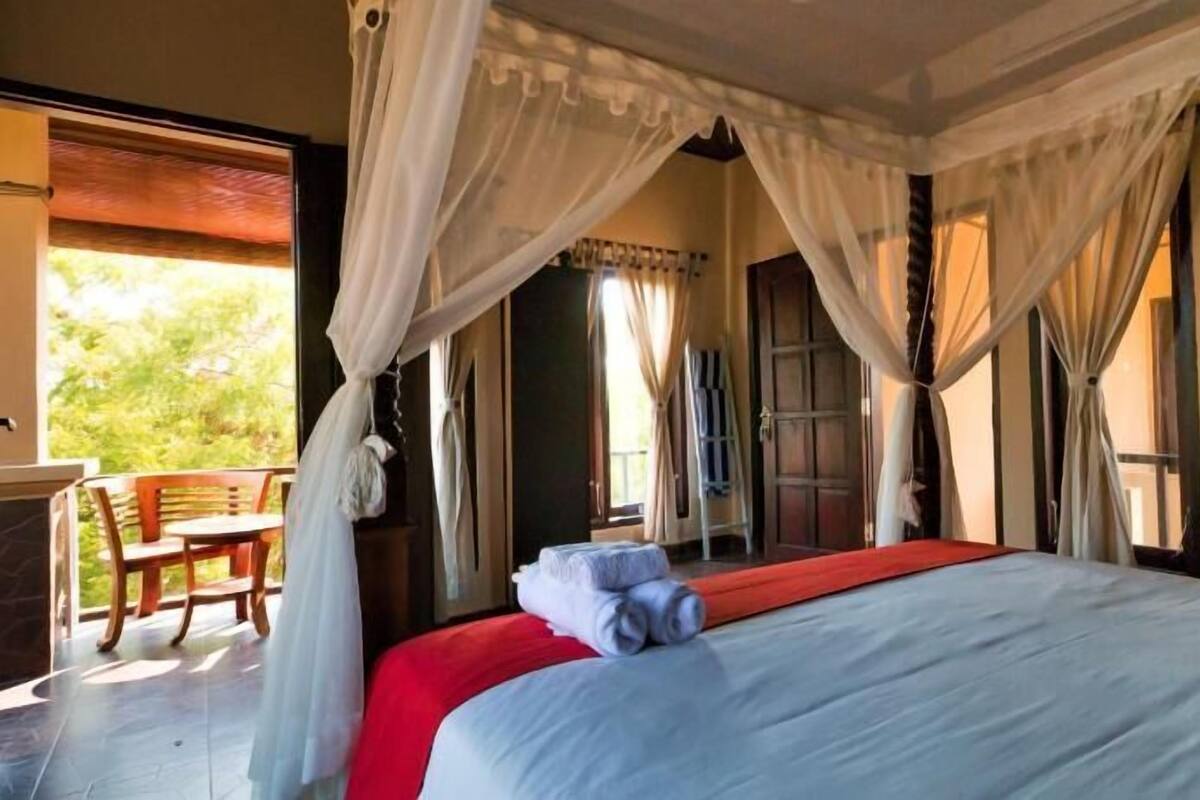 Una habitación con una cama, una silla y un ventanal con cortinas.