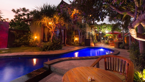 Ein Pool mit gewölbter Kante, umgeben von tropischen Pflanzen und einer Holzterrasse.