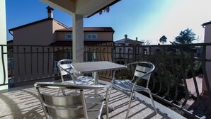 Ein Balkon mit Tisch und Stühlen, Blick auf angrenzende Häuser und einen klaren Himmel.