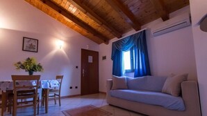 Ein Wohnzimmer mit Holzboden, einer Couch, einem Esstisch mit Stühlen und einem Fenster mit Vorhängen.