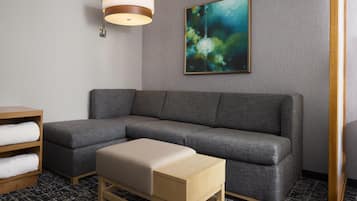 Ett modernt hotellrum med en grå, modulbaserad soffa, ett träbord, en beige pall, en abstrakt tavla som hänger på väggen och en hängande taklampa.