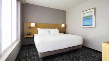 A hotel room with a large bed, two bedside tables with lamps, a nightstand, a framed picture on the wall, and a window providing natural light.