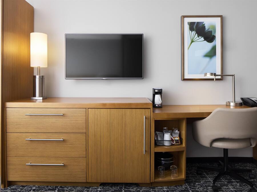 A hotel room with a wooden desk, a flat-screen TV, a lamp, a chair, and a framed picture on the wall.