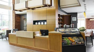 Un área de recepción moderna con un mostrador de madera, una vitrina con aperitivos y el logotipo de Starbucks en la pared.