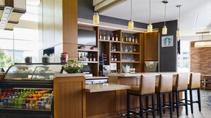 A modern bar area with wooden cabinets, a refrigerated display case, and bar stools. - Hyatt Place New York/Yonkers (Yonkers)