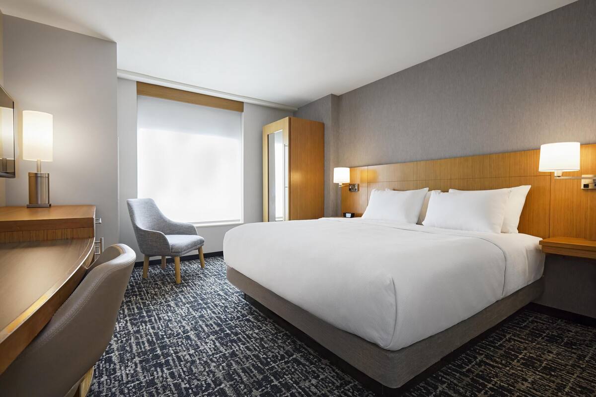 A hotel room with a large bed, a desk, a chair, and a window with curtains.