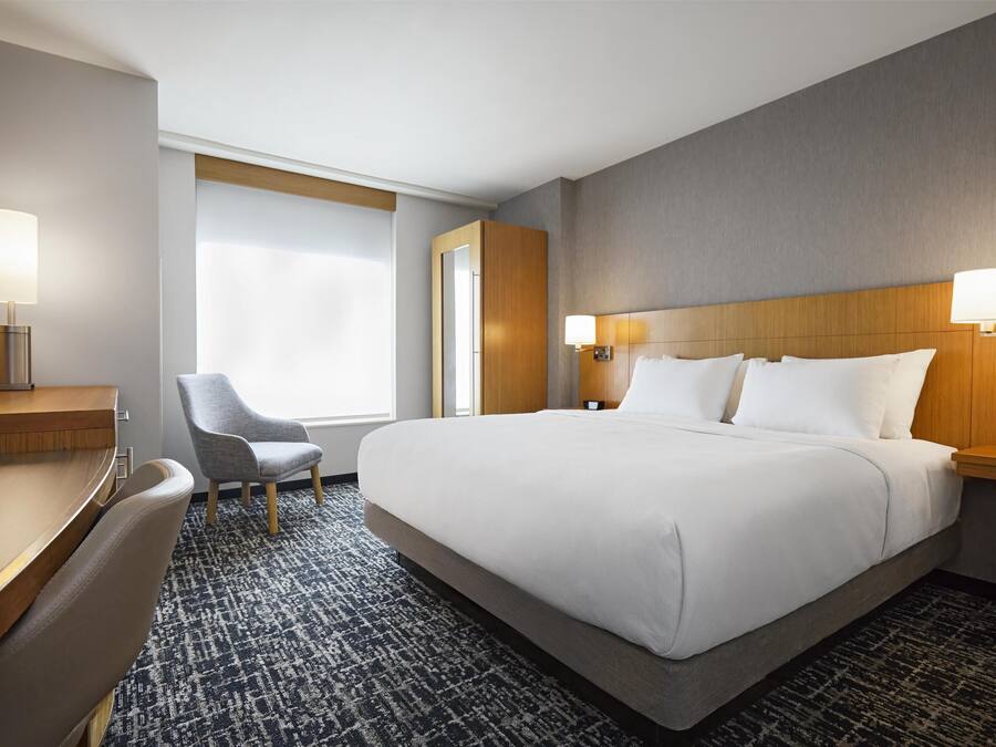 Habitación de hotel con una cama grande, un escritorio, una silla y una ventana con cortinas.