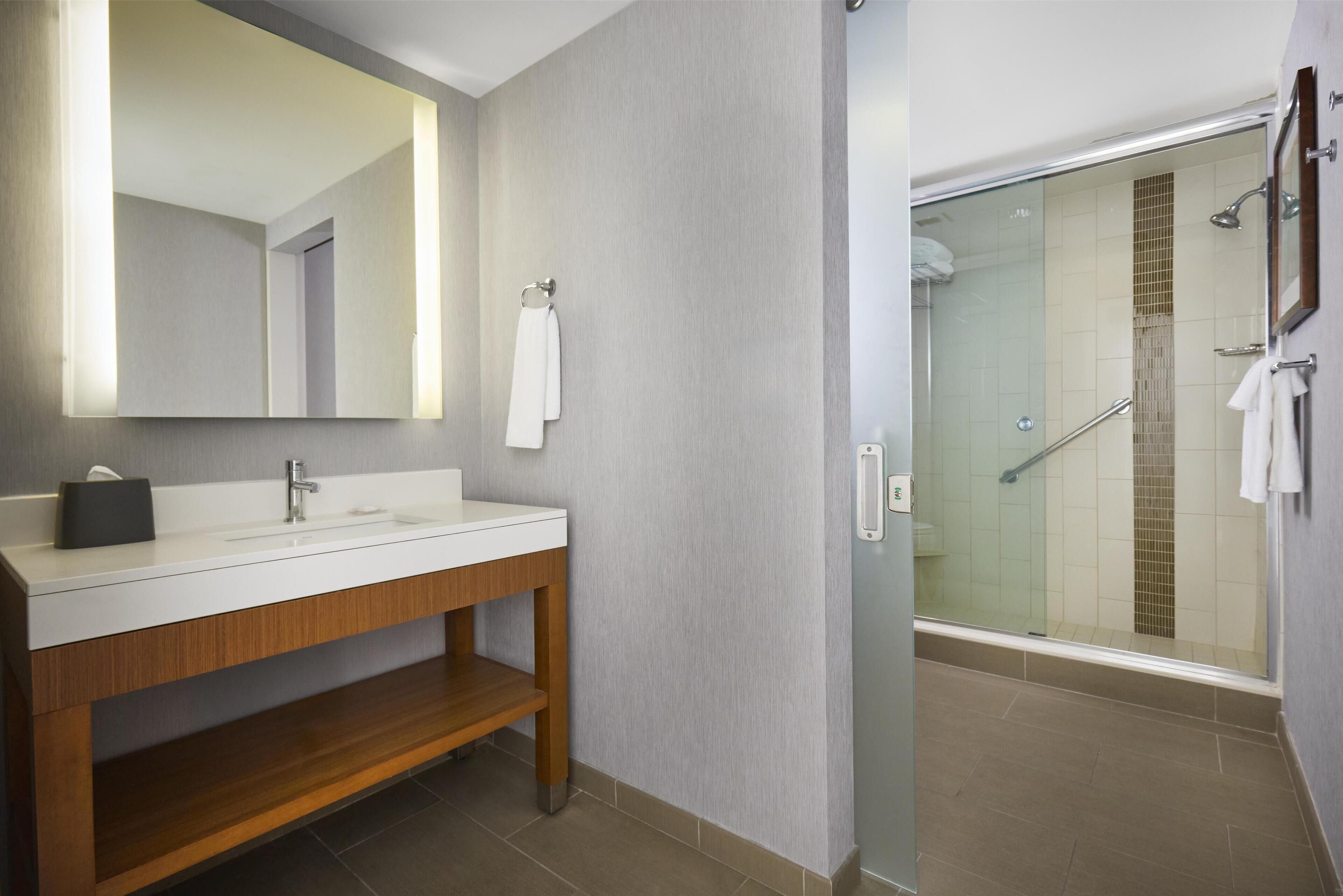 A modern bathroom with a wooden vanity, a large mirror, and a glass-enclosed shower area.