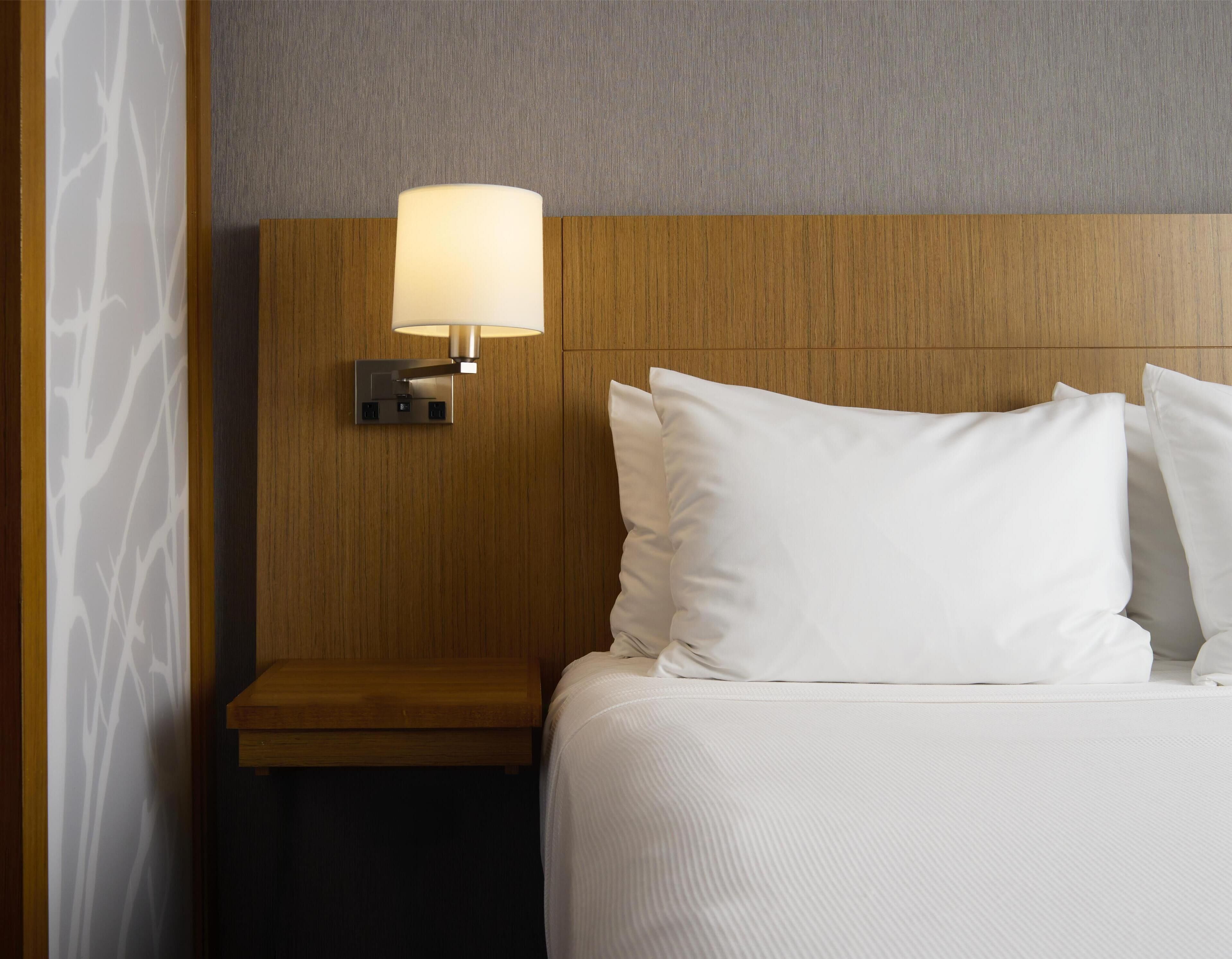 A hotel room with a wooden headboard, a bedside lamp, and white bedding.