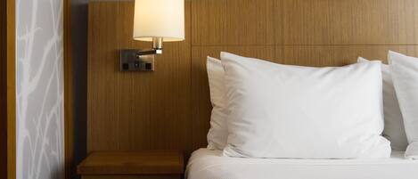 A hotel room with a wooden headboard, a bedside lamp, and white bedding.