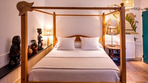 Uma cama com dossel com roupa de cama branca, cabeceira de madeira e uma mesa de cabeceira com objetos decorativos.