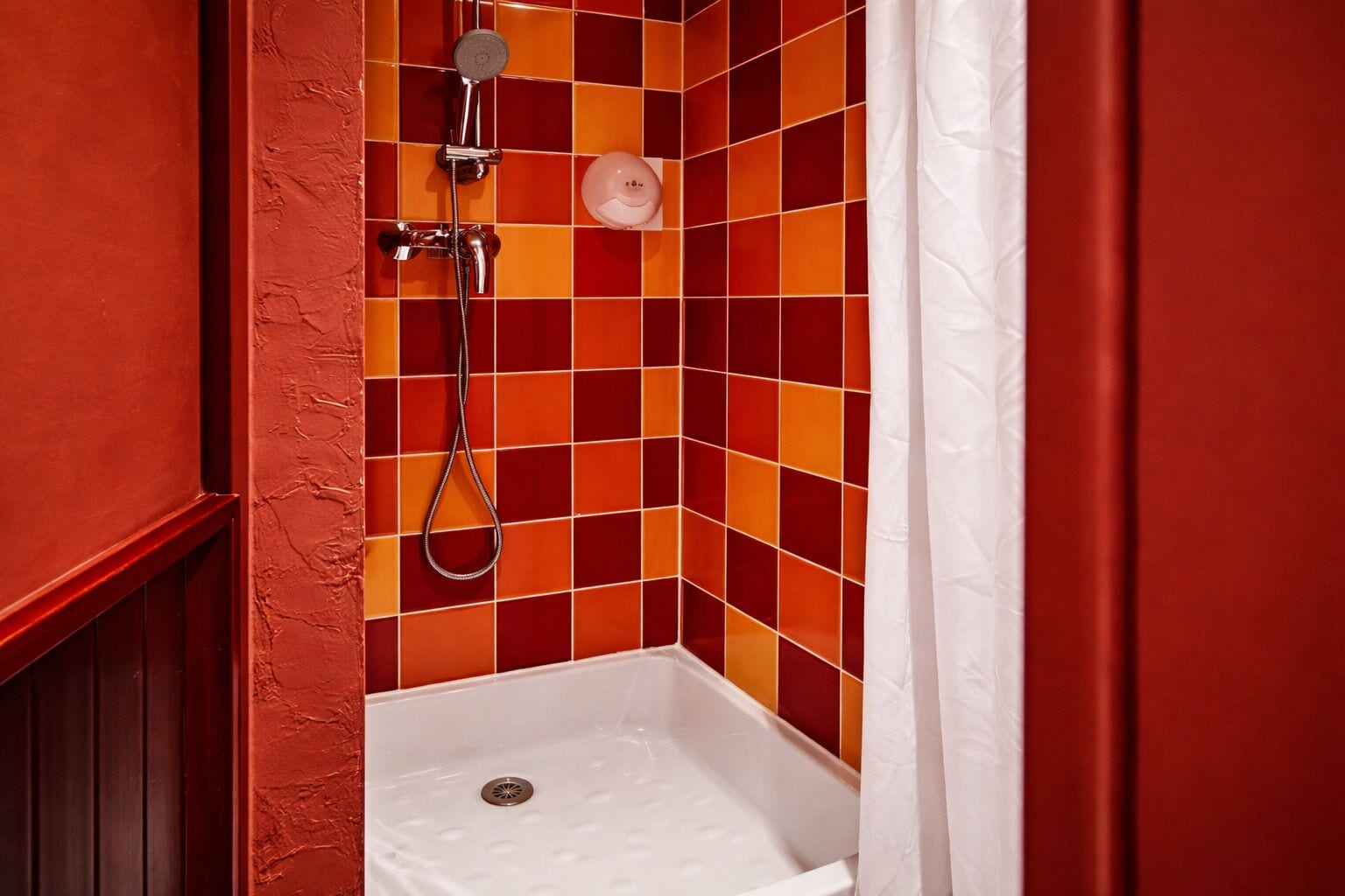 Un baño con ducha, una bañera blanca y un revestimiento de azulejos con un diseño rojo y naranja.