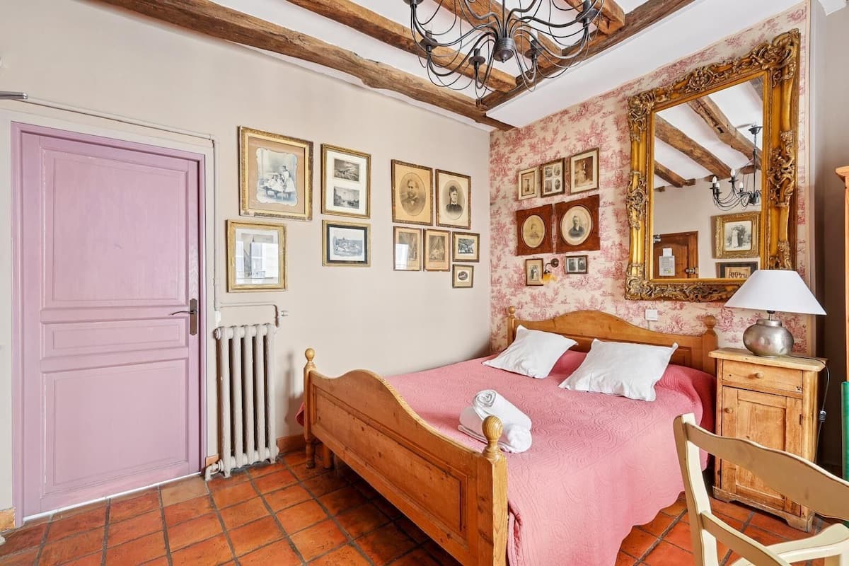 A bedroom with a wooden bed, a pink door, a radiator, and a mirror with a floral frame.