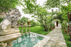 A stone fountain with a lion sculpture, surrounded by potted plants and a clear pool. - Hotel de Nesle (Paris)