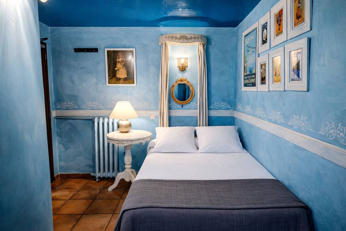 A bedroom with a bed, a nightstand, a lamp, a mirror, and framed pictures on the wall.