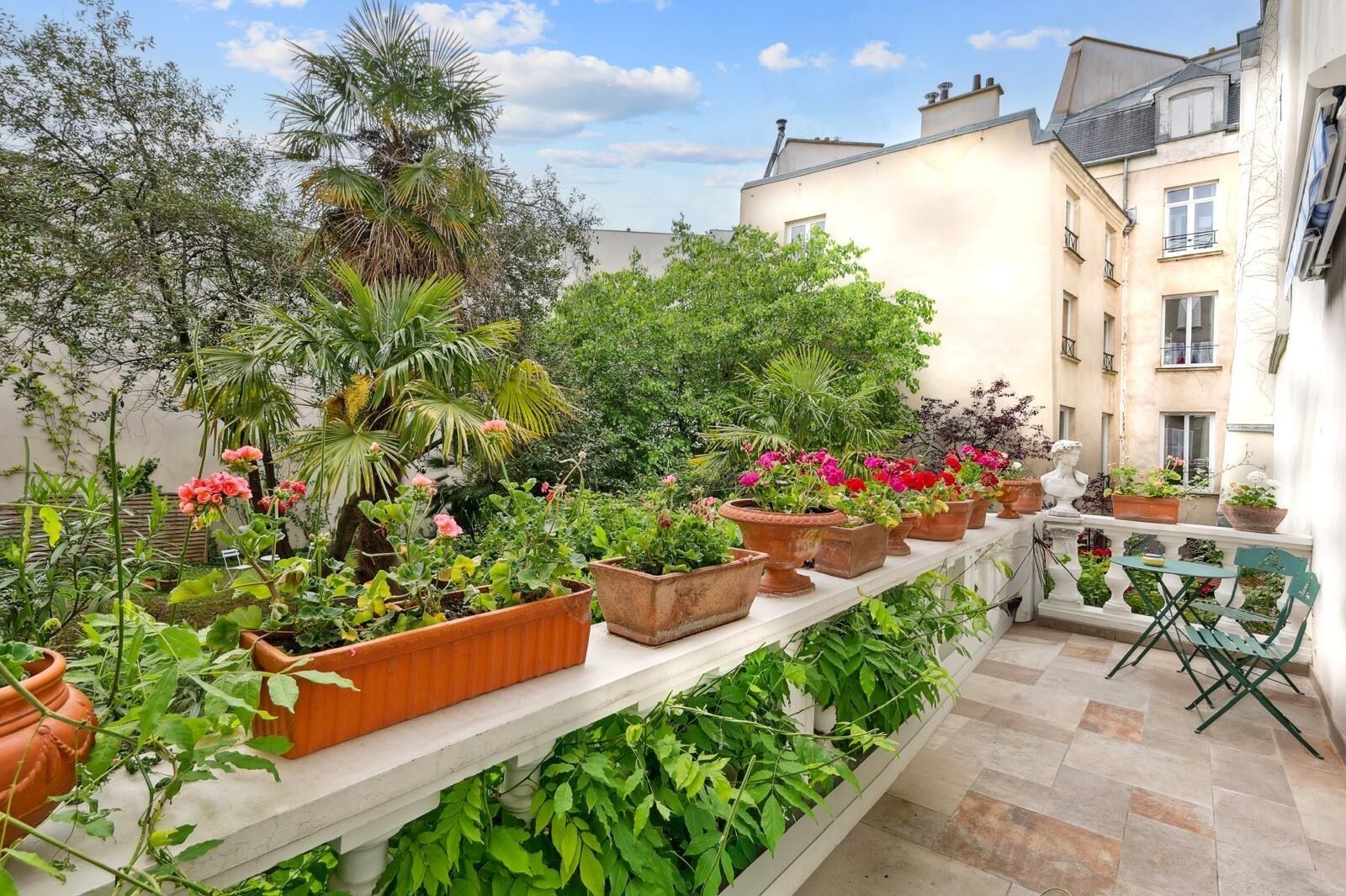 A balcony with potted plants and a small table with chairs.