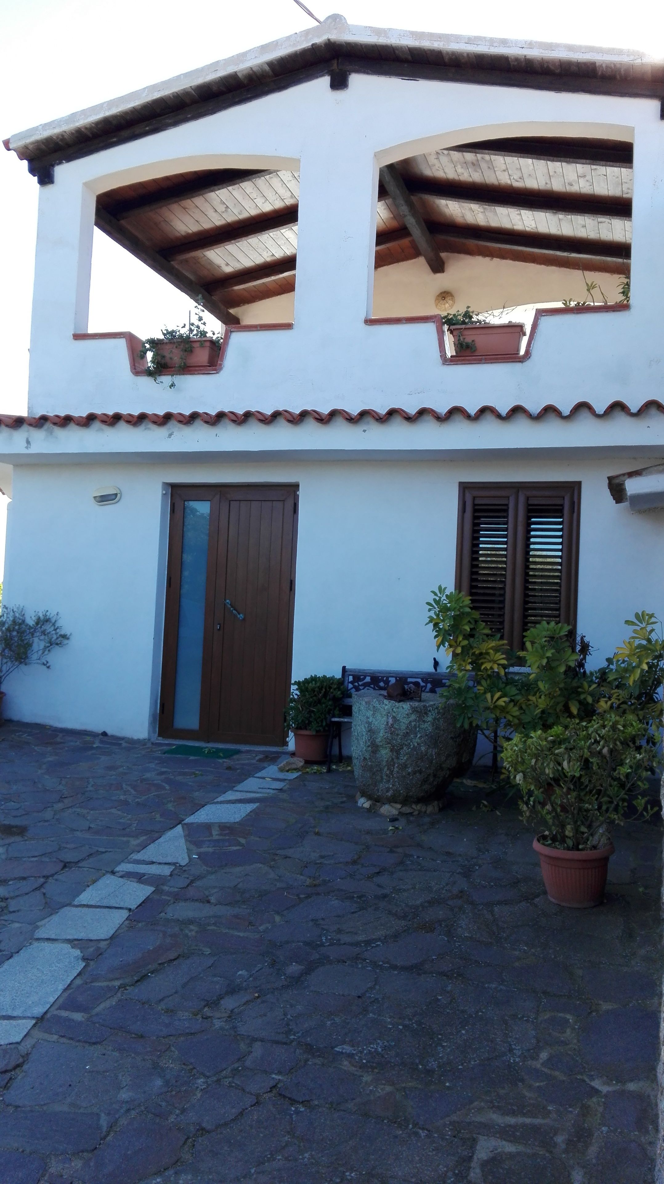 A two-story building with a tiled roof, a wooden door, and potted plants.