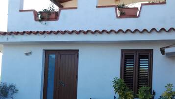 A two-story building with a tiled roof, a wooden door, and potted plants.