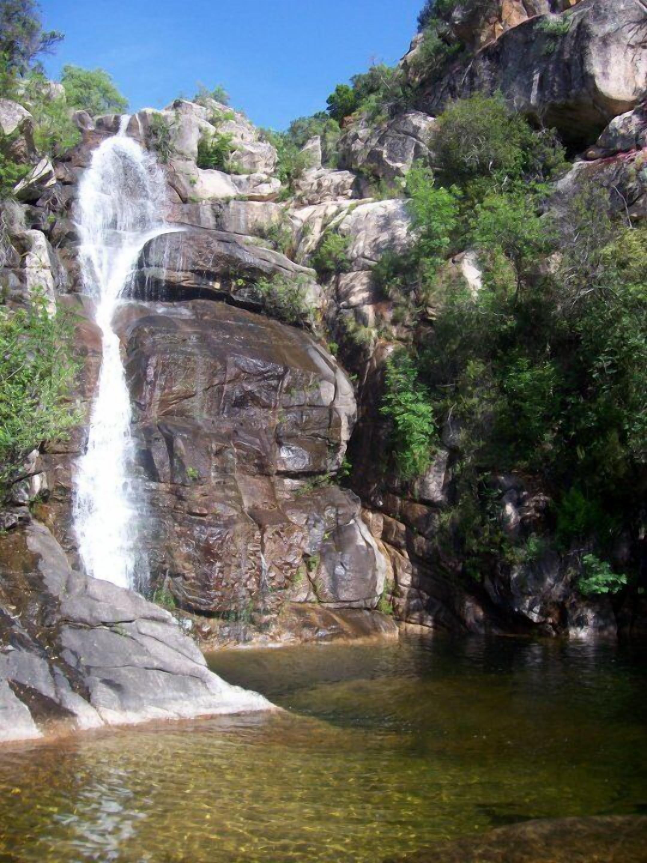 A waterfall cascading over rocky terrain with a clear pool at the base.