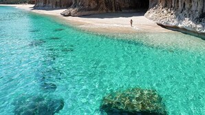 A clear turquoise sea with a rocky cliff and a sandy beach.