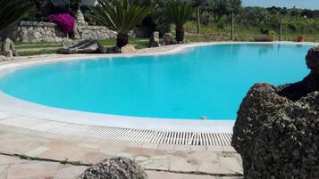 A swimming pool with a stone deck, surrounded by rocks and plants.