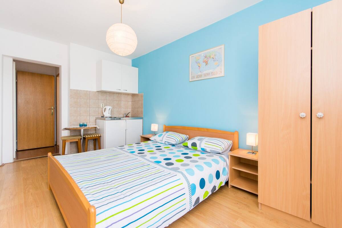 A bedroom with a bed, bedside tables, a wardrobe, and a kitchenette.