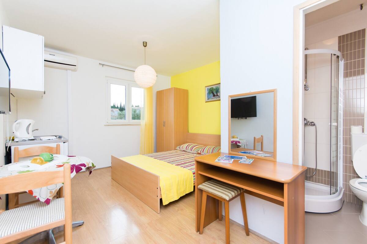 A bedroom with a bed, desk, chair, and a shower area.