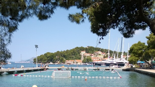 A waterfront marina with boats, a swimming area, and a building in the background. - Nina Apartments (Konavle)