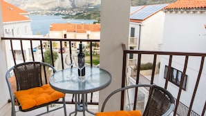 A balcony with wicker chairs, a glass table, and a bottle of wine. - Nina Apartments (Konavle)