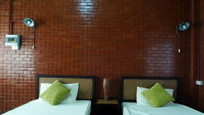 Ein Zimmer mit zwei Betten, jedes mit einem grünen Kissen, vor einer Ziegelwand.