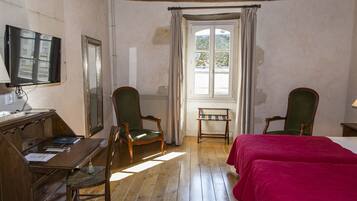 Una habitación con muebles de madera, una cama con cubrecolor rojo, un escritorio con computadora y una ventana con cortinas.