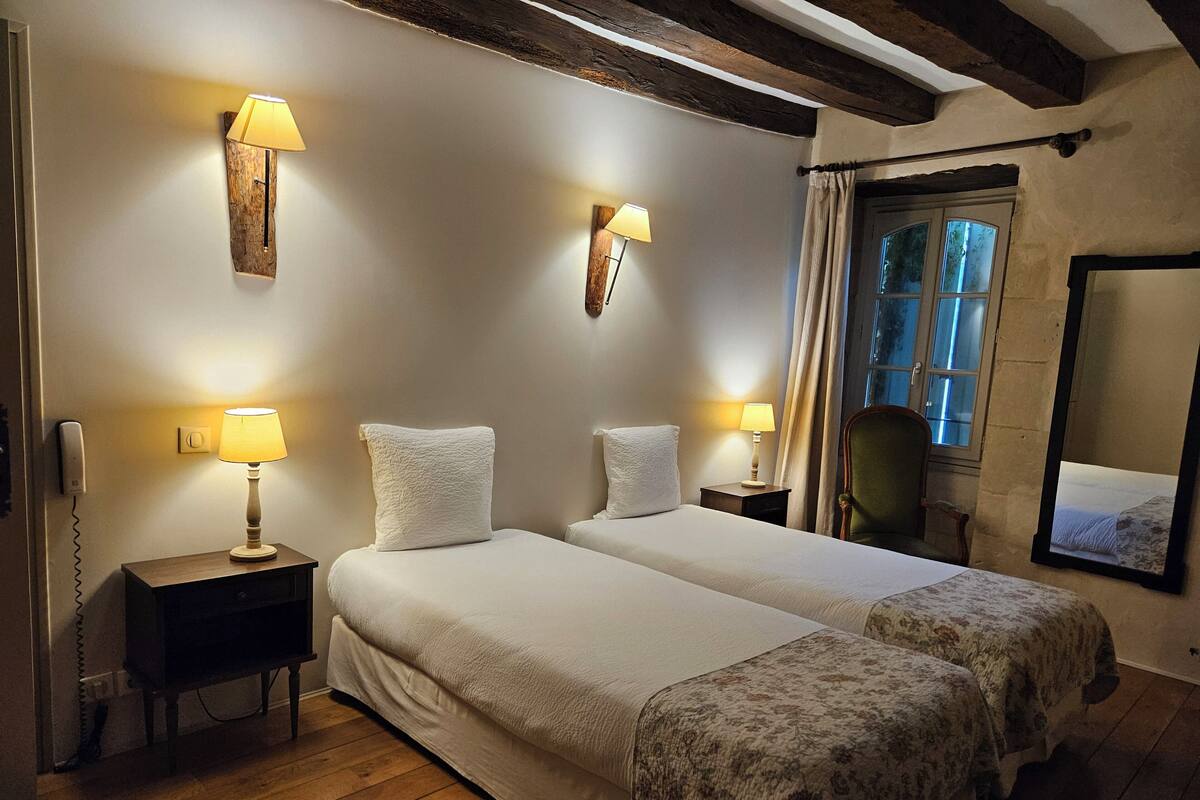 Een hotelkamer met twee bedden, houten vloeren en een grote spiegel aan de muur.