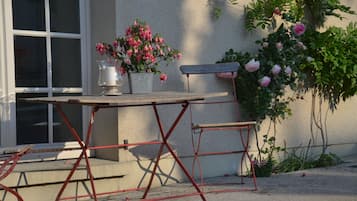 Un patio con una mesa, sillas, una planta en maceta y un banco fijado a la pared.