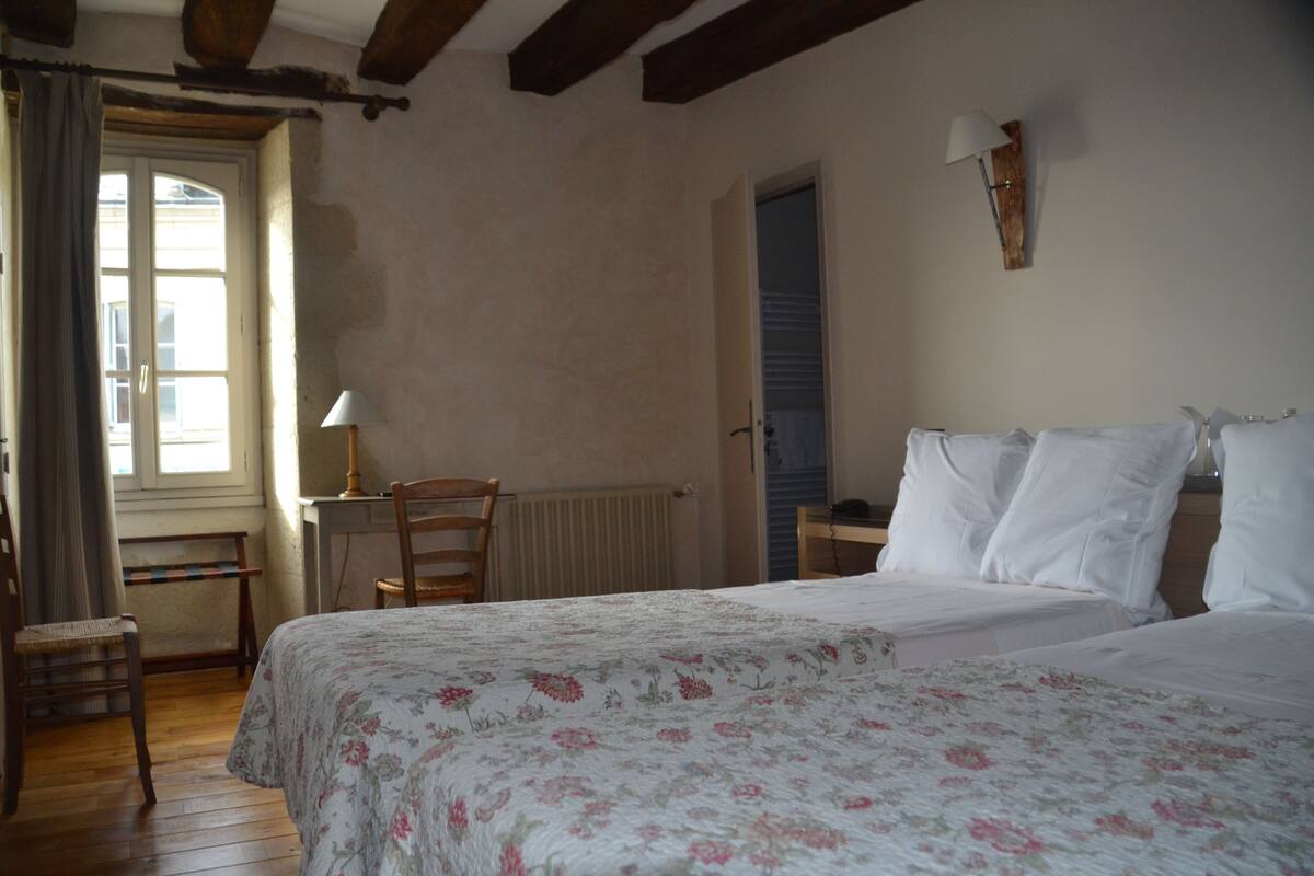 Een slaapkamer met een bed, een stoel, een bureau en een raam met gordijnen.