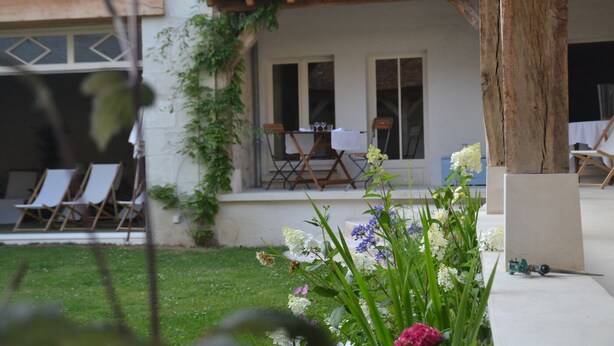 Ein Gebäude mit einer überdachten Terrasse, Sitzgelegenheiten im Freien und einem Blumengarten.