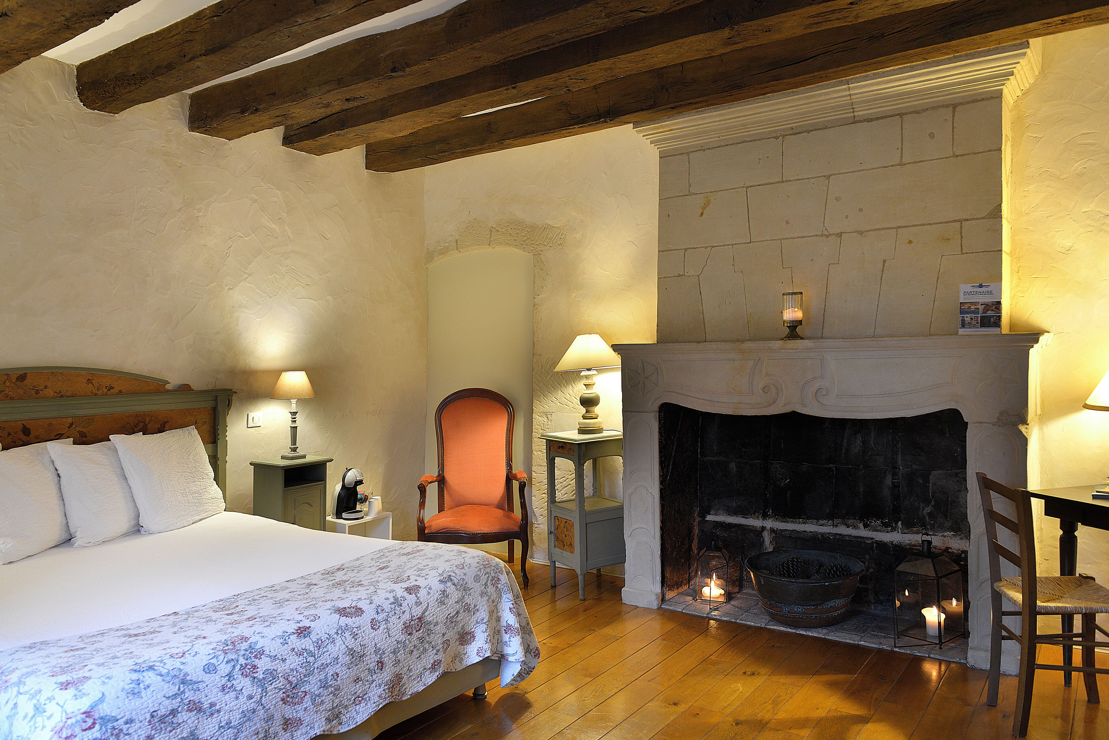 A bedroom with a bed, a chair, a table, a fireplace, and a nightstand.