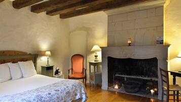 A bedroom with a bed, a chair, a table, a fireplace, and a nightstand.