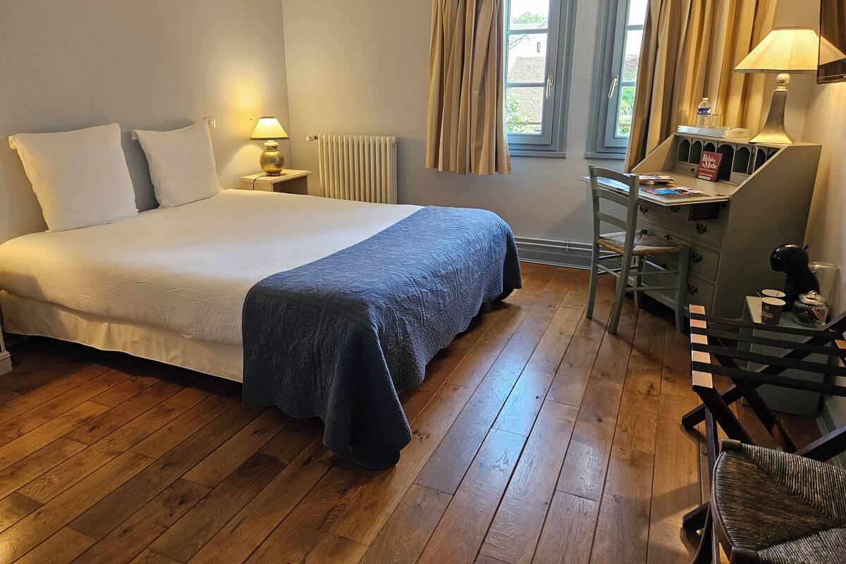 Een netjes ingerichte slaapkamer met een groot bed, een bureau met stoel en een raam met gordijnen.