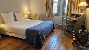Un dormitorio ordenado con una cama grande, un escritorio con silla y una ventana con cortinas.