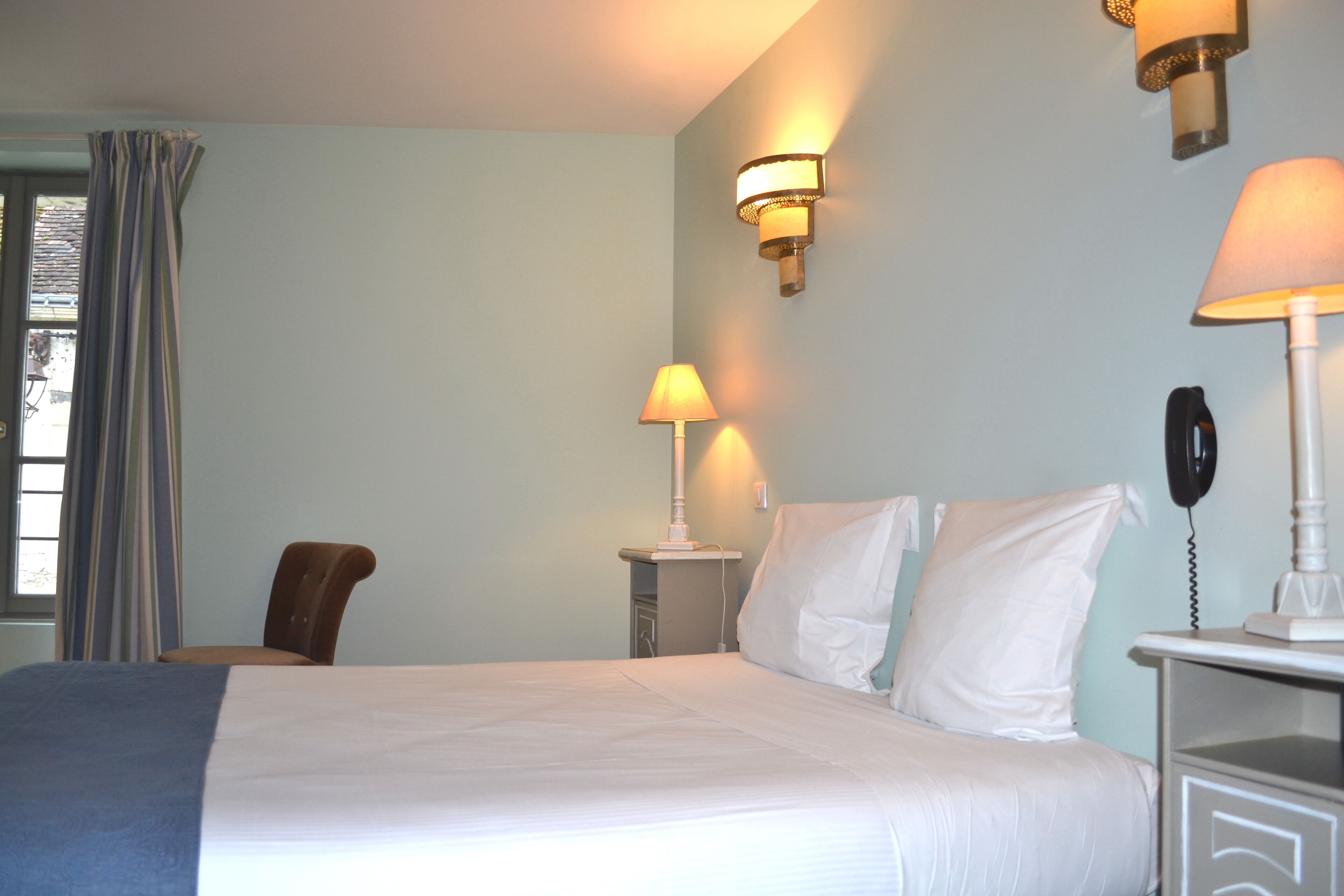 A hotel room with a bed, two bedside lamps, a chair, and a nightstand with a phone.